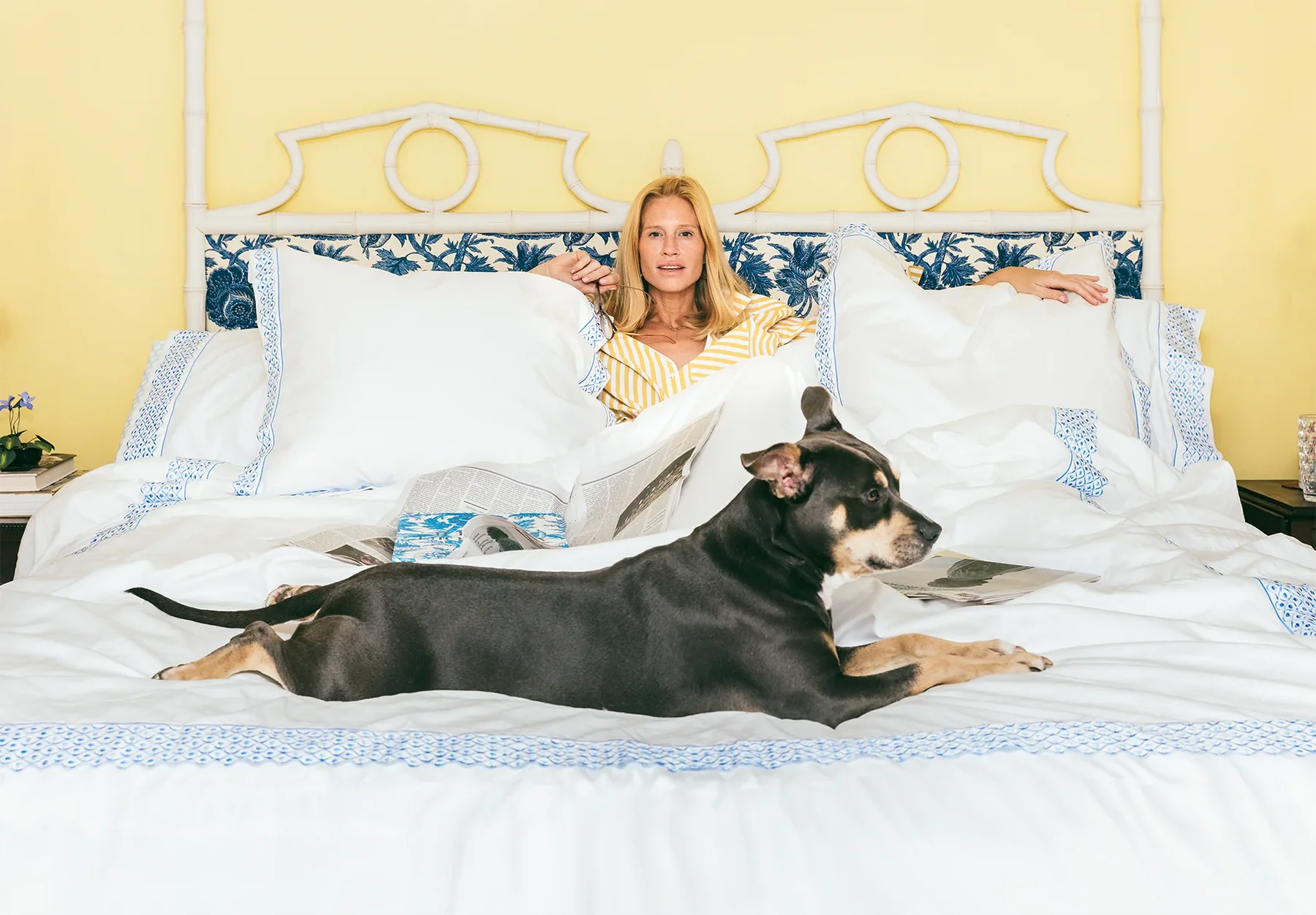 Woman lying in bed with a dog on a yellow bedroom background