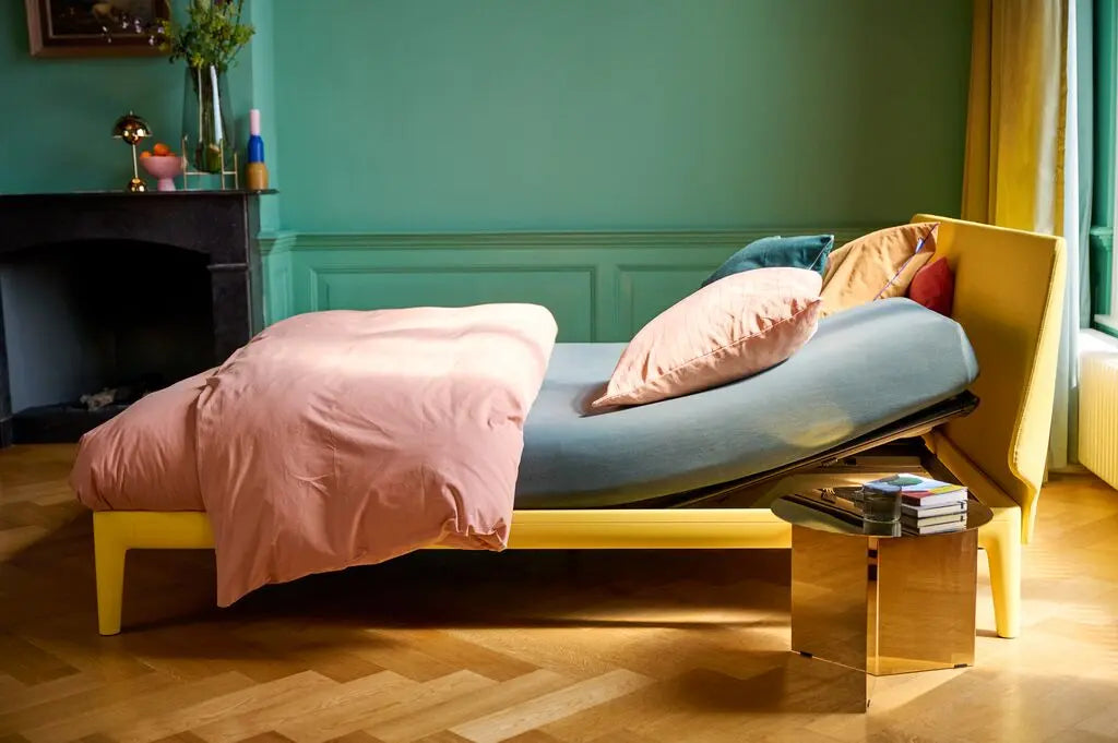 Auping essential Bed with pink bedding in a room with teal walls and a yellow chair.
