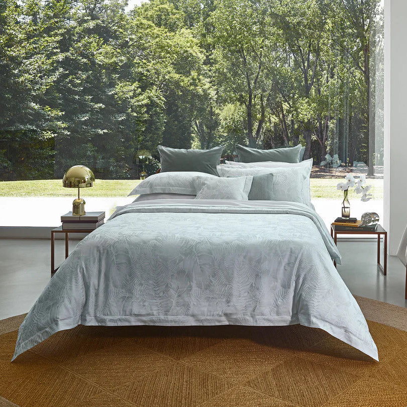 Modern bedroom with a bed equiped with copacabana duvet cover and pillowcase sham jade, chair, and large windows overlooking trees
