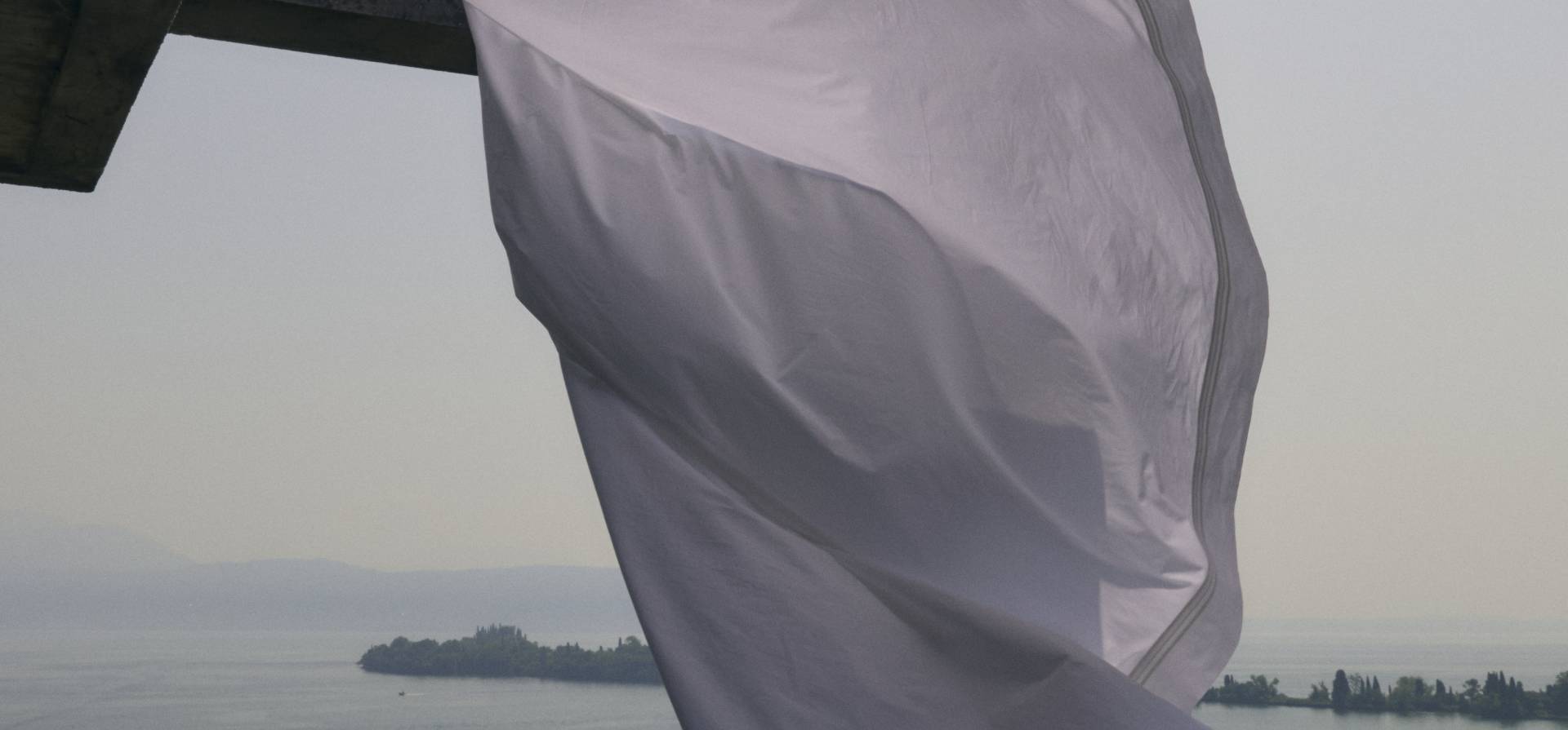 White fabric flowing in the wind with a scenic background of water and trees.